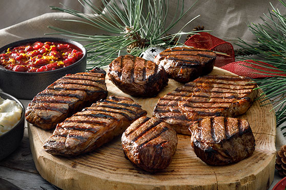 different cuts of grilled steak arranged on cutting board with side dishes